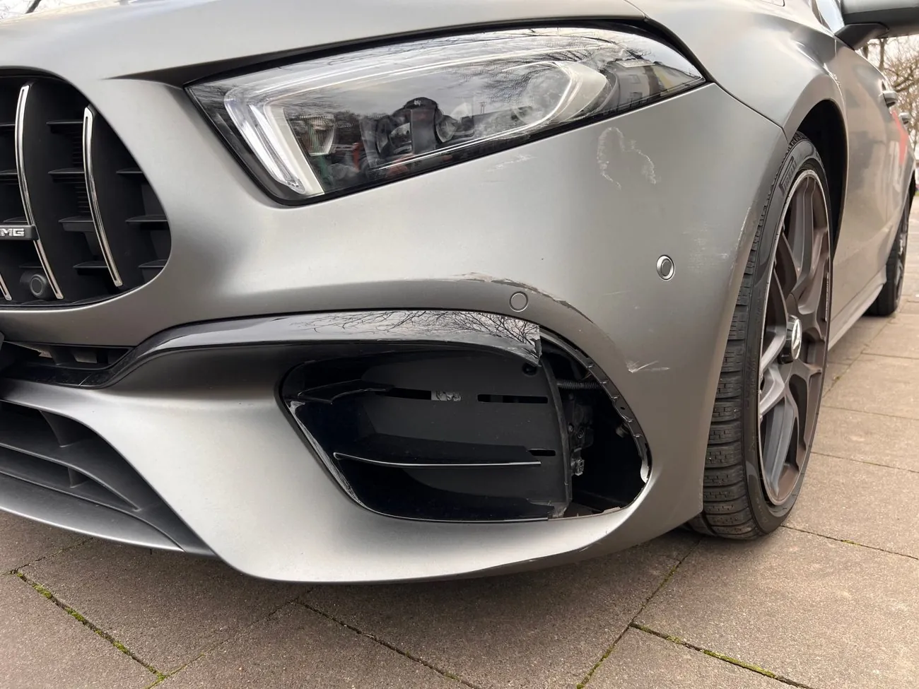 Frontschaden an einem grauen Mercedes mit abgerissener Stoßfängerverkleidung