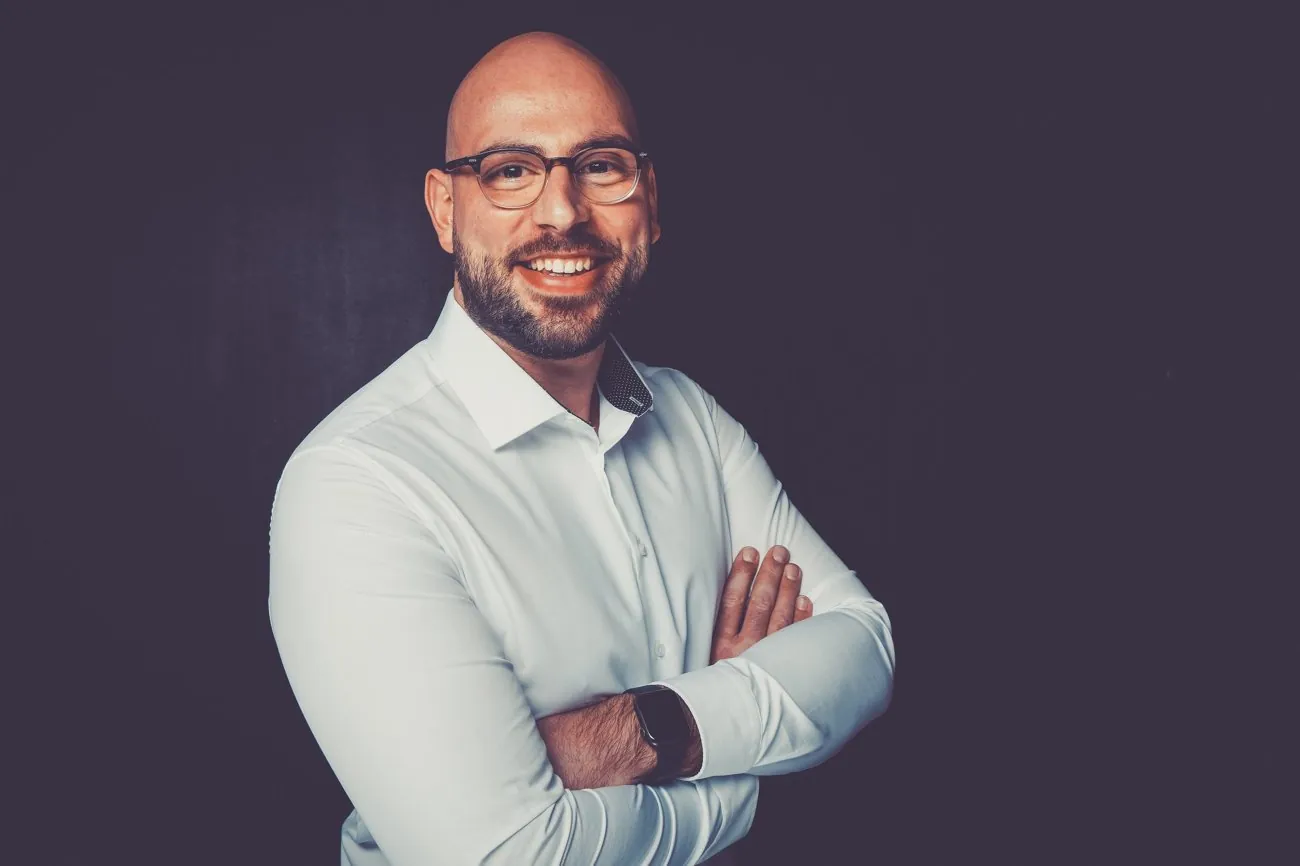 Onur Karagöz, Kfz-Sachverständiger aus Köln, mit verschränkten Armen vor dunklem Hintergrund